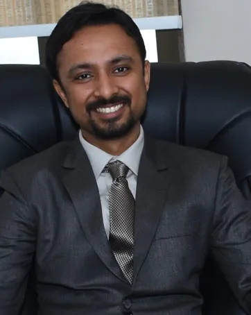 Man in a gray suit and tie sits in a black leather chair, smiling at the camera.